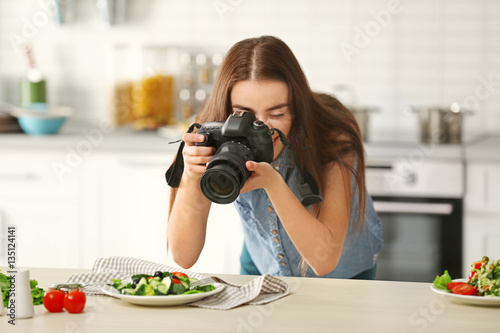 Young pretty woman photographing food in kitchen