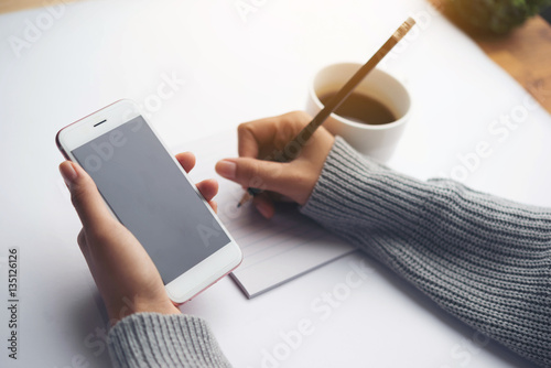 Female hand writing down on letter paper with cup of tea on the wood desk, top view