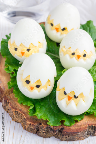 Little chicken in nest, deviled eggs served with salad on wooden board, vertical