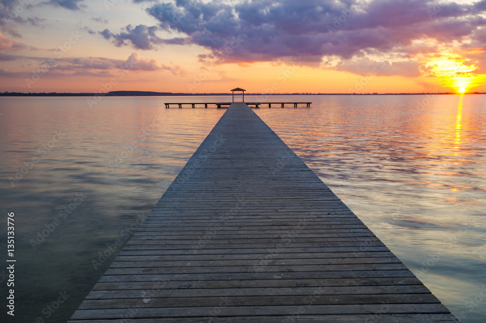 Obraz premium wooden pier overlooking the lake, the beautiful evening sky, colored by the setting sun 