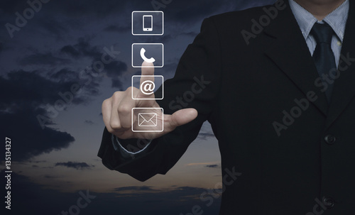 Businessman pressing telephone, mobile phone, at and email buttons over sunset sky, Customer support concept
