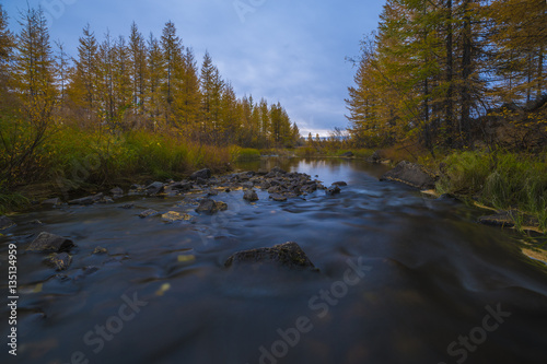 Fall autumn day landscape with river, forest, clouds on the blue sky and sun.