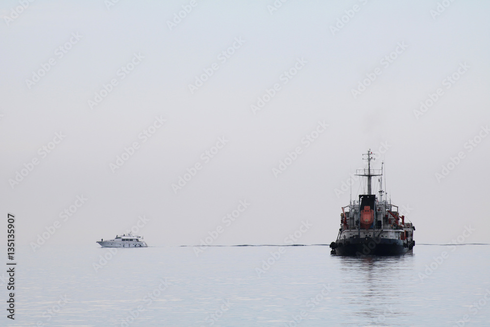 Fototapeta premium A small boat and big ship on calm sea water in fog