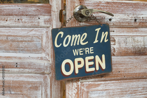Sign Come In We're Open hanged on the wooden door, retro style.