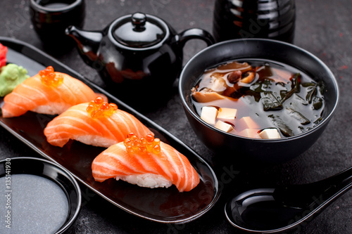 Japanese cuisine. Salmon sushi nigiri and miso soup on black plate a dark table.