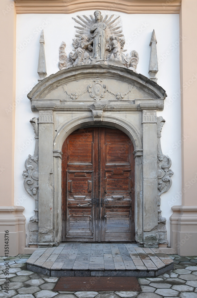 Arched wooden door of an old stone building with decorative carved elements. Church of St. Brigid, Grodno, Belarus.