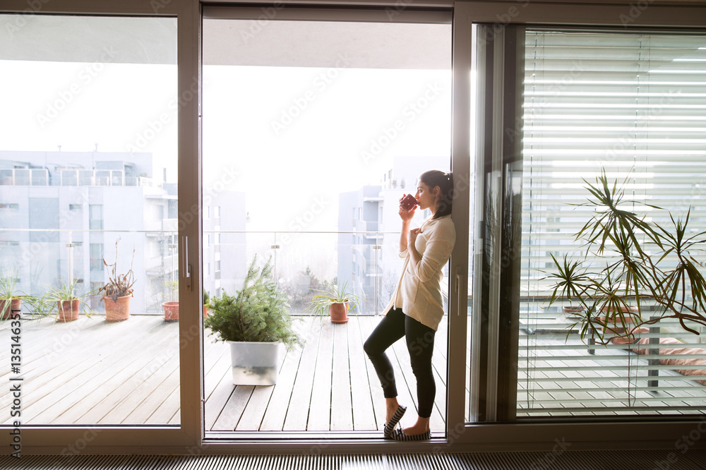 Woman relaxing on balcony holding cup of coffee or tea - obrazy, fototapety, plakaty 