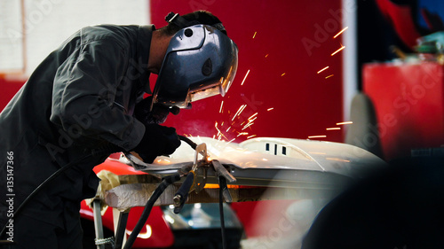 Fotografie Welding industrial: worker in helmet repair detail in car auto service