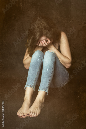 Crying shy girl sitting on the ground. Curled up woman with face in hands photo