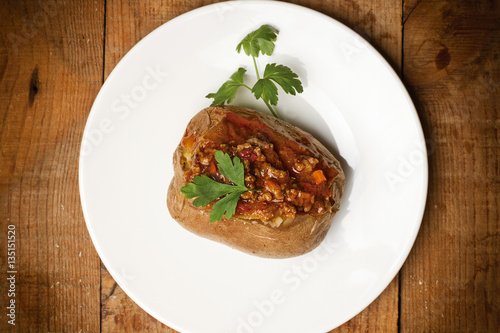 Patata rellena sobre plato blanco redondo sobre mesa de madera rústica. Vista superior