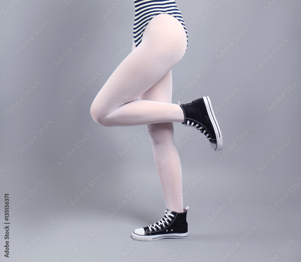 Woman in white tights and sneakers on gray background Stock Photo