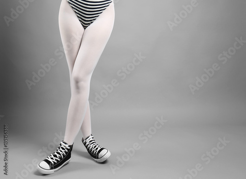 Woman in white tights and sneakers on gray background