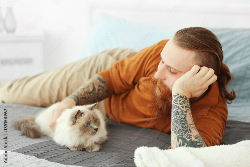Young bearded man with fluffy cat lying on bed Young bearded man with fluffy cat lying on bed