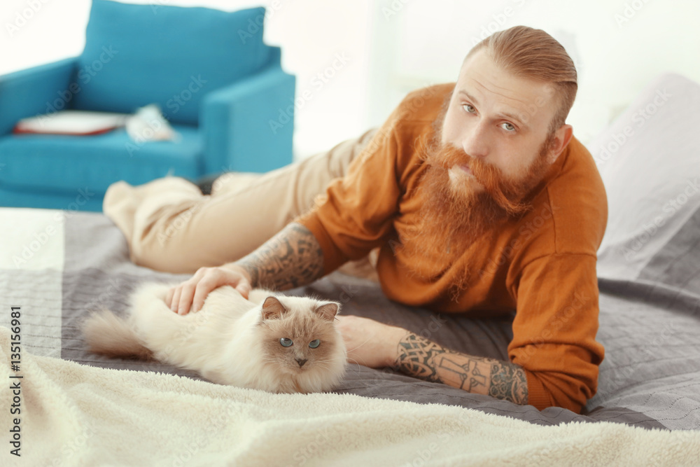 Young bearded man with fluffy cat lying on bed Young bearded man with fluffy cat lying on bed