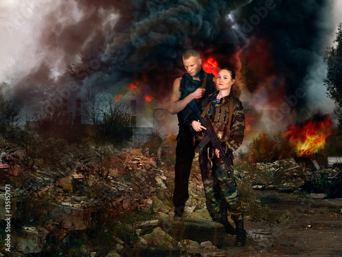 girl and man in military camouflage uniforms among the ruins of a fire in the background.
