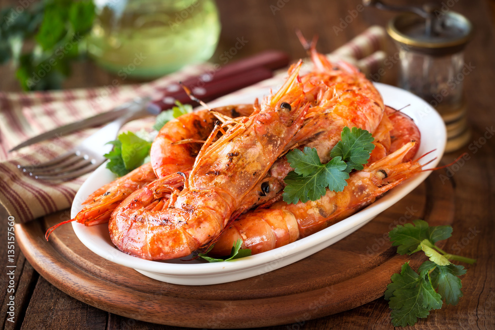 Grilled King prawns or shrimps with parsley on white plate on dark rustic wooden table Grilled King prawns or shrimps with parsley on white plate on dark rustic wooden table