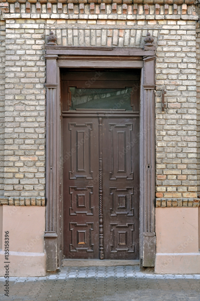 Brown framed vintage wooden door in a brick wall.