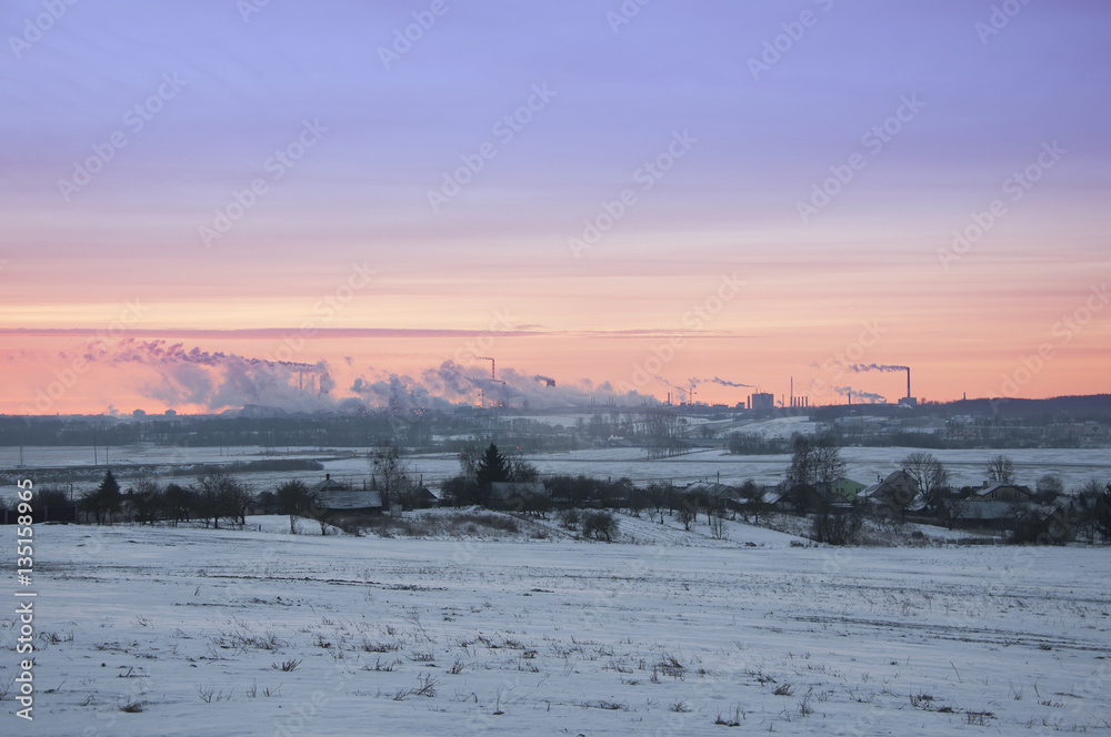 Working Nitrogen Plant in smoke on the background of dawn in winter. Abandoned village in the foreground. Grodno, Belarus.