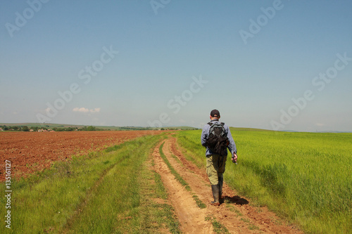 A man is walking on green wheat field and blue sky in spring time