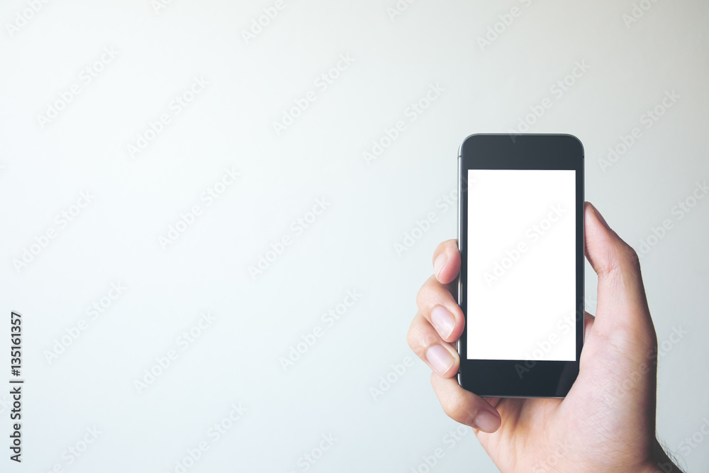 Mockup image of hand holding black mobile phone with blank white screen on white background room