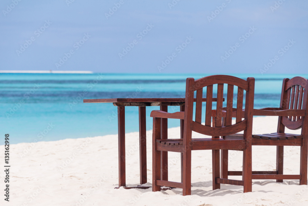 wooden table with two chairs on tropical beach with turquoise water in background