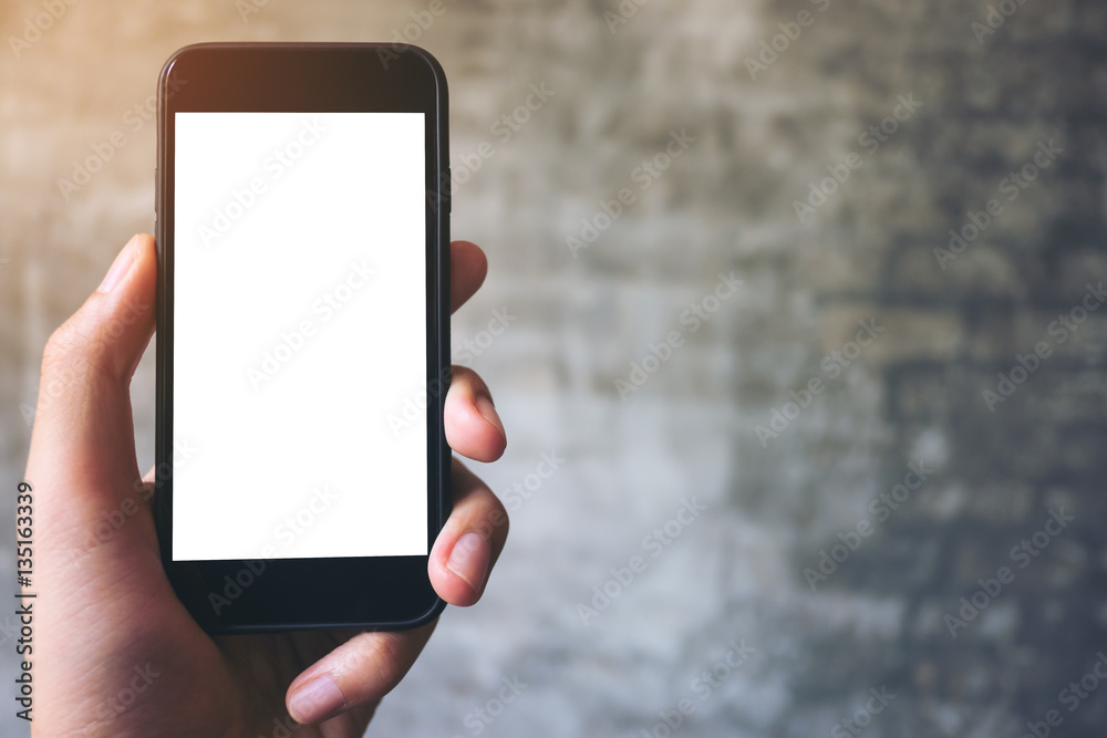 Mockup image of hand holding black mobile phone with blank white screen on concrete polishing wall background 