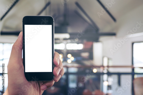 Mockup image of hand holding black mobile phone with blank white screen in cafe
