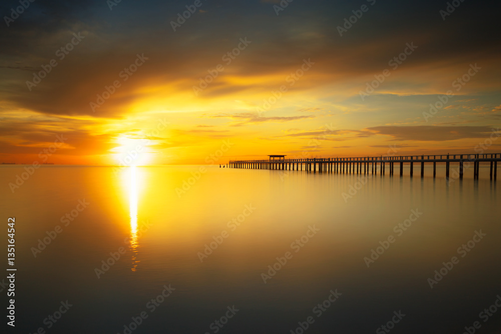 Wooden bridge into the sea at sunset