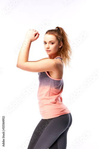 Portrait of a young athletic woman with a beautiful body relief. Teenager doing fitness. Sports as a hobby. The girl in a pink shirt and black tight sweat pants demonstrates arm muscles. © alexmishchenko