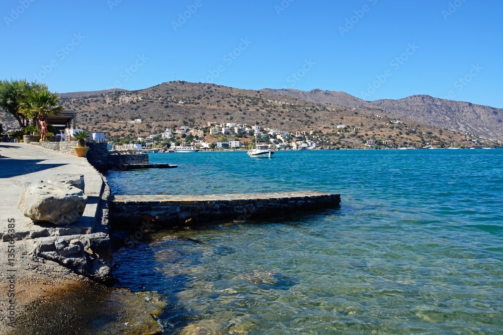 View across the bay towards the coastline with the rocky shoreline in the foreground, Elounda, Crete.