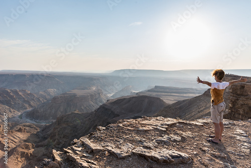 Rear view of tourist looking at expansive view over the Fish River Canyon, scenic travel destination in Southern Namibia. Ultra wide angle view from above.