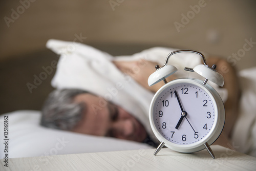 Waked Up Man lying in bed turning off an alarm clock in the morning
