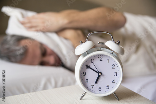 sleeping man disturbed by alarm clock early morning. Sleepy mature man