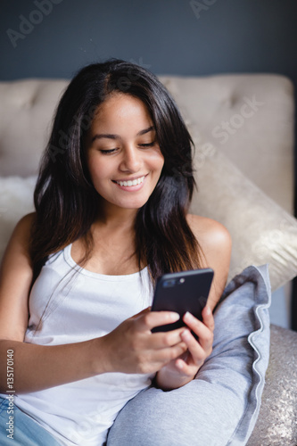 Teen girl using cellphone one bed
