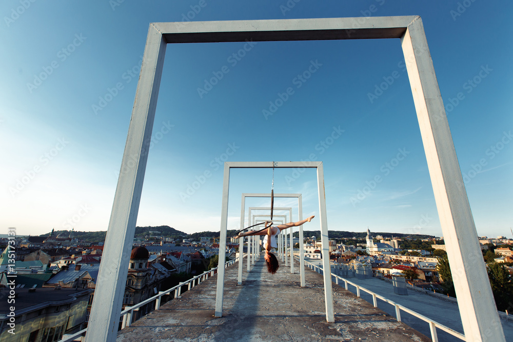 Sexy strong dancer performing on aerial hoop on rooftop