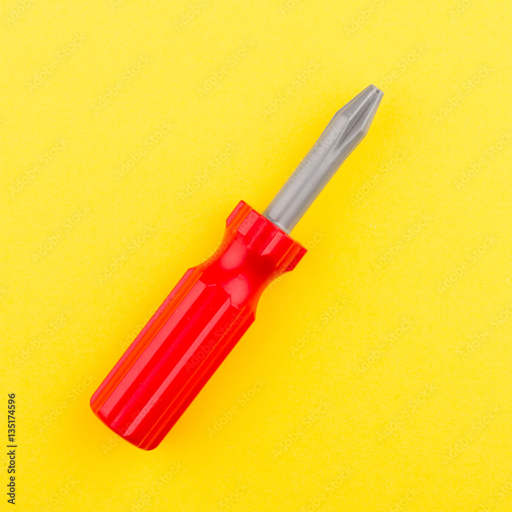 red plastic toy screwdriver on yellow background red plastic toy screwdriver on yellow background