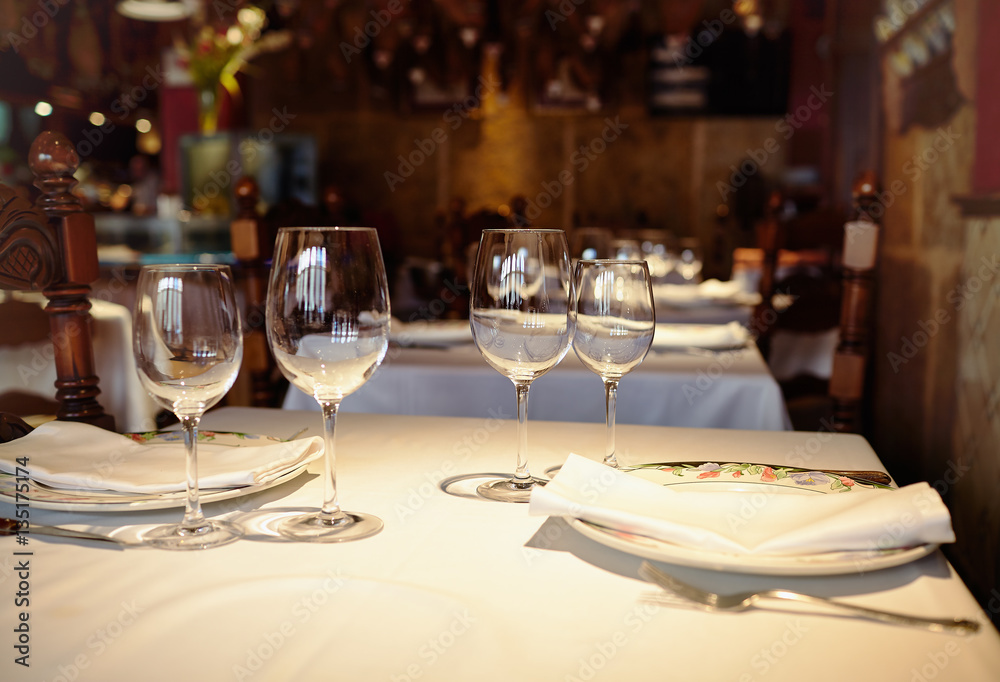 Empty glasses in a restaurant on white tablecloth. Shade, brown background and carved chairs.