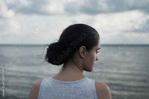 Sensual portrait of young beautiful brunette woman posing against the background of sky and water.