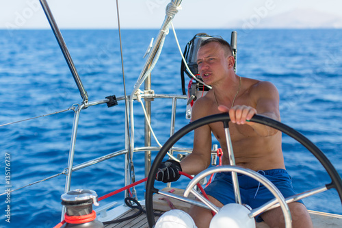 Man skipper at the helm controls of a sailing yacht. © De Visu