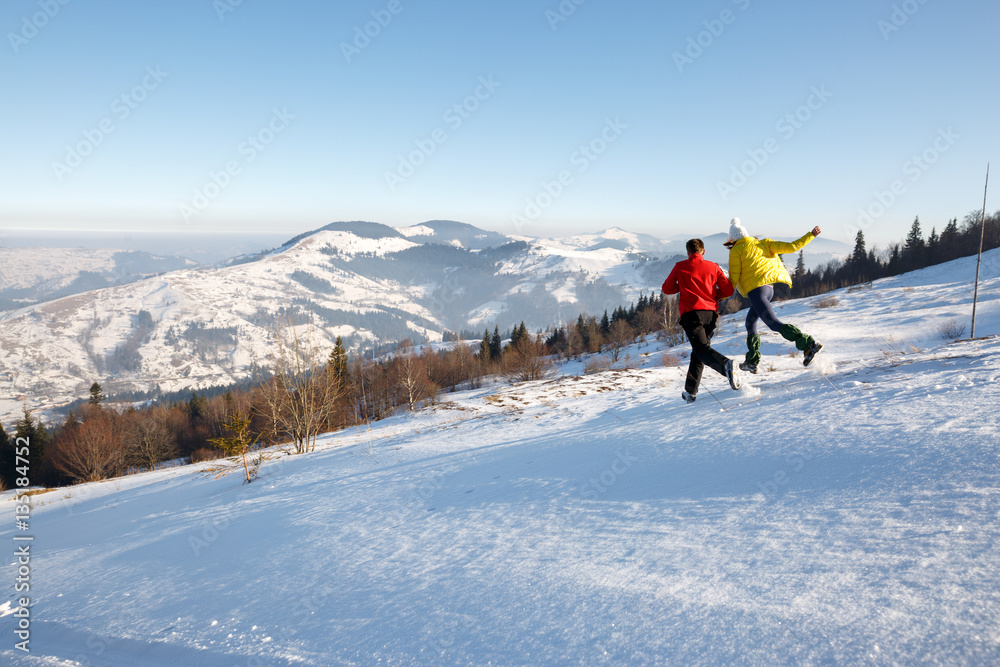 Young couple hiking outdoors with backpacks in winter mountains