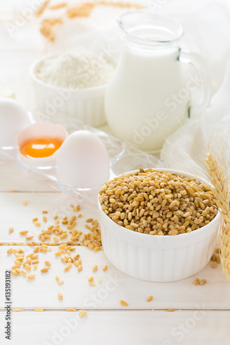 Ingredients for baking: flour, milk, wheat grain, butter and eggs on white wooden background. Selective focus   © thayra83