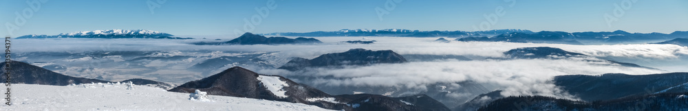 Panorama from top of winter mountain ridge above low clouds