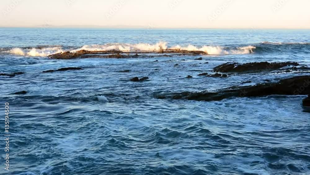 Waves along a rocky beach crash and swirl over a shallow offshore reef system during a morning sunrise. Waves along a rocky beach crash and swirl over a shallow offshore reef system during a morning sunrise.