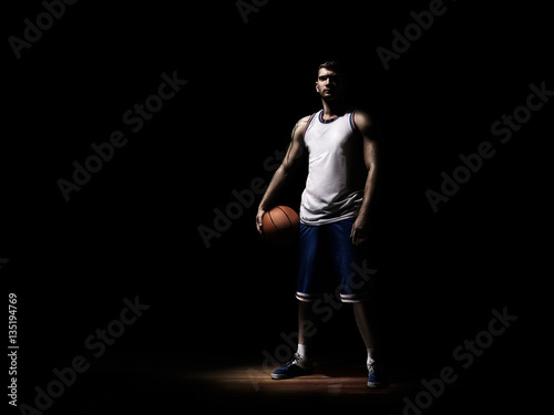 basketball player standing in durkness on parquet with ball