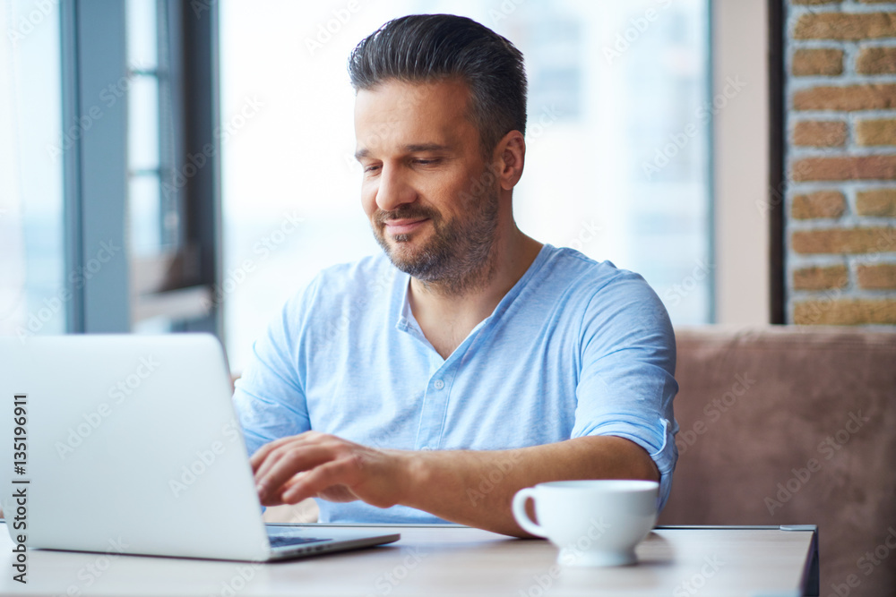 Handsome man with cup of coffee using laptop at home Handsome man with cup of coffee using laptop at home