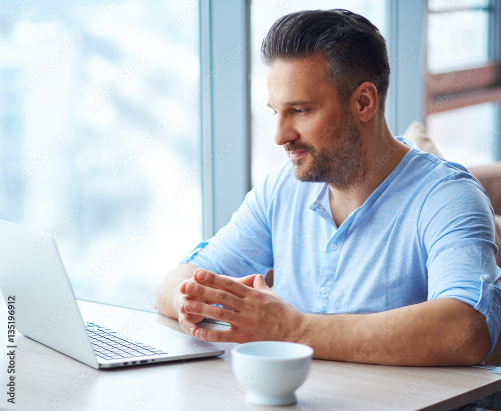 Handsome man with cup of coffee using laptop at home Handsome man with cup of coffee using laptop at home
