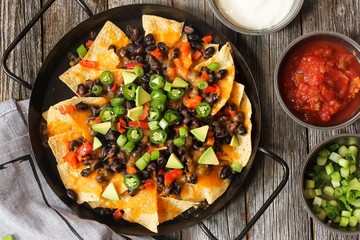 Classic Nachos with Tortilla chips melted cheese sauce jalapeno peppers avocado salsa and sour cream / Game day food