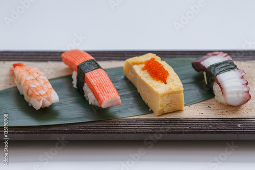 Sushi Set Include Shrimp, Kani, Tamagoyaki with Squid Served on Leaf on Stone Plate.