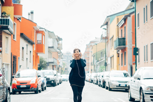 Young beautiful caucasian brown hair woman outdoor in the city listening music with head phones, and smart phone hand hold - technology, music, relaxing concept