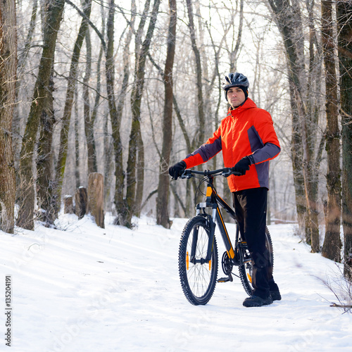 Mountain Biker with Bike on the Snowy Trail in Beautiful Winter Forest